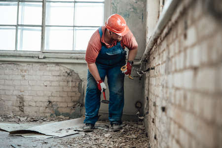 Professional worker in a safety helmet strikes old plaster from brick wallの写真素材