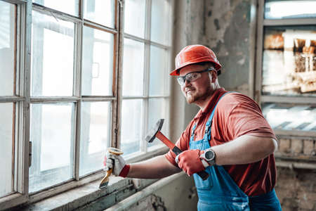 Professional worker, in uniform and goggles, beats old plaster from a brick wallの写真素材