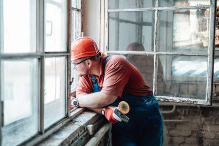 A tired builder looks out of the window of an old building, where he works as a contractorの写真素材