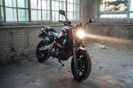 Black motorcycle, parked on the background of a brick wall and many glass windows, at an abandoned...