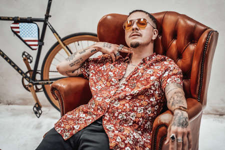 Very expressive and stylish guy in hawaiian shirt and sunglasses relaxing on a luxury retro sofa looks like freakly gangsterの写真素材