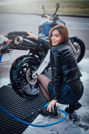 An owner enjoying by taking care about his vehicle. Happy woman near her sport bike. Car wash service.の写真素材