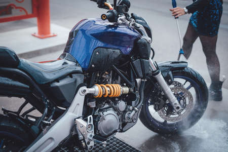 Dark casual motorcycle are taking care by the girl. Woman cares about her bike. Glow and illuminated photo in car wash service.の写真素材