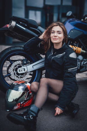 Young cute female driver and dark modern bike. Urban powerfyl vehicle. Motosport hobby.