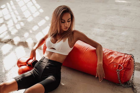 Young and sensitive sportswoman with long hair posing in a light studio sitting on the floor with an...