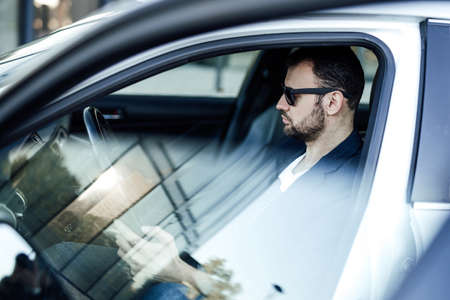 A rich guy looking at his smartphone. Modern car and his owner which using his phone. A foreign car in the street.の写真素材