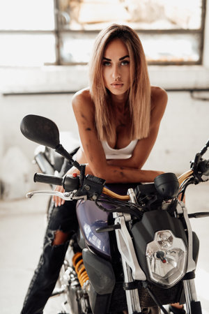 Beautiful female biker sitting on a custome made urban motorcycle in white garage. A repairing job...