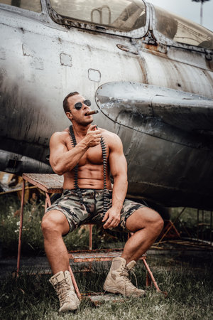 USA soldier discovered abandoned plane. Bodybuilder in military fashion smoking cigarette and...
