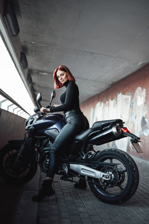 A female sexy biker dressed in black with her sport motorbike. Woman likes her motosport hobby.