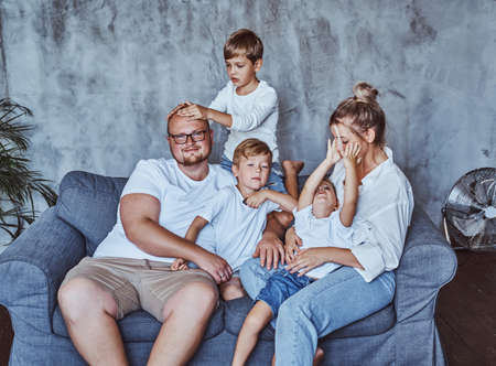 Positive family of wife husband and three boys resting and having a good time in their blue cool room.の写真素材