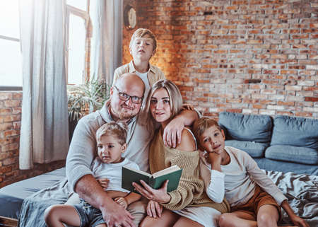 American happy family of wife husband and three boys resting and reading a book in hotels living room.の写真素材