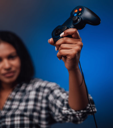 Looking schoolgirl blackskinned gamer grips modern device of console. Feminine gaming and youth...