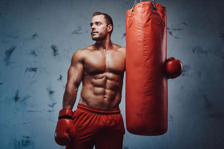 Handsome bodybuilder with strong hands which protected with boxing gloves posing with punching bag.の写真素材
