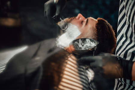 Modern and vintage barbershop with dark stylish brickwalls and barber which preparing his client for haircut.の写真素材