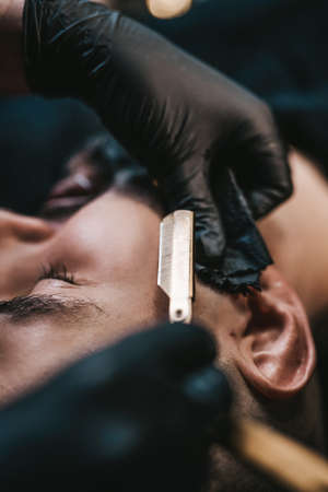 Adult guy is shaving by professional and skilled barber in stylish and modern saloon.