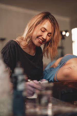 Female and caring tattoo master cleaning her clients shoulder using a doily in warm and shiny salon.の写真素材