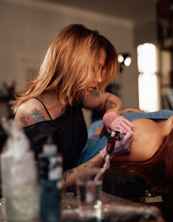 Warm photography of female tattoo master which paints waves on shoulder of her customer in comfortable workplace.の写真素材