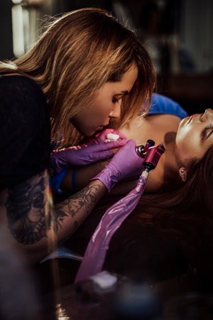 Warm photography of female tattoo master which paints waves on shoulder of her customer in comfortable workplace.の写真素材