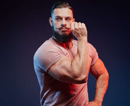 Stylish and muscular sportsman with beard touching his mustache and posing in dark background.の写真素材
