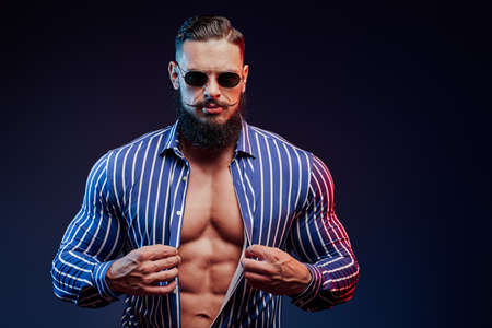 Succesful and muscular bearded guy showing his perfect abs and posing in dark background.の写真素材