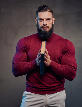 Elegenace mature guy in sweater with muscular body and beard posing holding book in gray background.