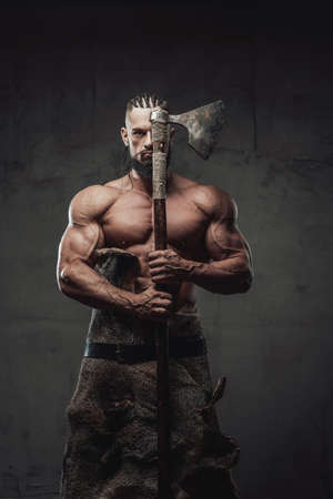 Brutal and powerful viking warrior with dreadlocks and beard posing with axe which covers half of his face in dark background.の写真素材