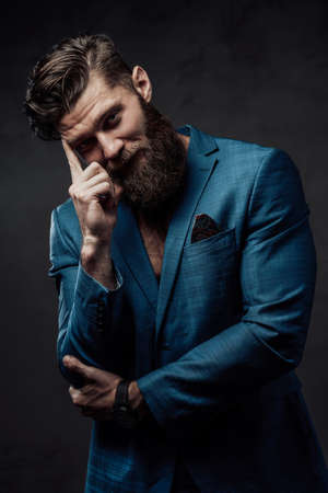 Brutal and handsome man with beard and stylish haircut posing with finger to his head in dark background.の写真素材