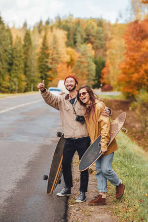 Embracing and joyful girl and guy stopping cars and going to rest after walking in lovely and golden autumn forest.の写真素材