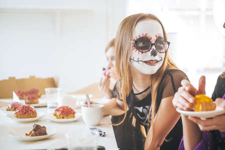 Preschool girls with make up and custom clothing eating some sweets at the halloween party in shiny dining room.の写真素材