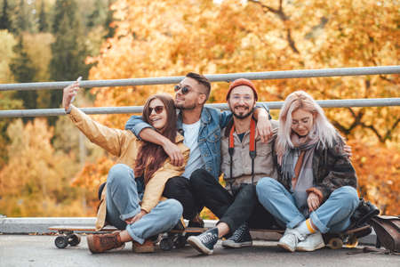 Peaceful autumn park and group of two boys and two girls they are relaxing and photographing on skates in daytime.の写真素材