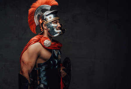 Armoured and serious imperial militray roman posing dressed with steel helmet and red mantle looking away in dark background.の写真素材