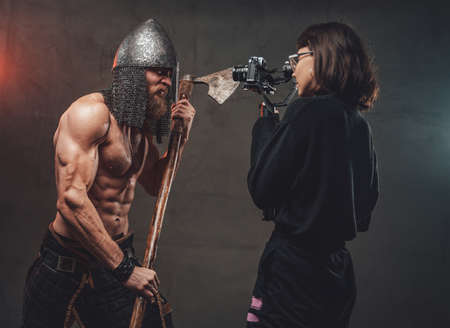 Shirtless and muscular guy with axe and helmet in fashion of savage viking poses for camera while photographer shots him.の写真素材