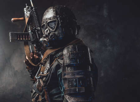Apocalyptic survivor dressed in custom armour and helmet poses holding his gun in dark background.の写真素材