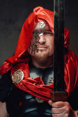 Headshot of roman soldier he dressed in black armour and mask with red hood he holds sword in dark...