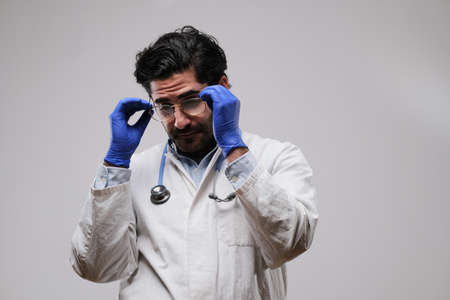 Mature doctor dressed in white coat with rubber gloves wearing his glasses in white background.の写真素材