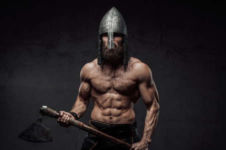 Strong and furious nord barbarian posing in dark studio background holding his two handed axe on hands.の写真素材