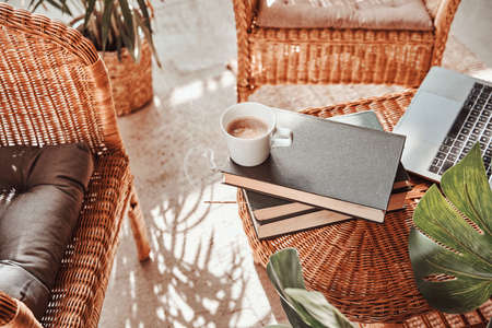 A warm and soft hotel room with a custom design table with a coffee cup and books on it and bamboo chairs with pillows.の写真素材