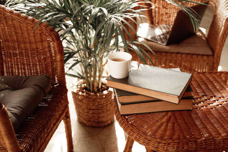 Warm and soft hotel room with custom design table with coffee cup and books on it and bamboo chairs with pillows.の写真素材