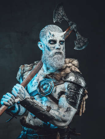 Evil fashion of king of the dead with naked torso and pale skin in dark background with two handed axe on his shoulder.の写真素材
