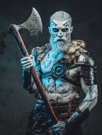 Shirtless and risen from the dead warrior with iced skin and horns in dark armour holding two handed axe in dark background.の写真素材