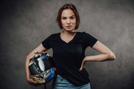 Glamour and self confident female motorcyclist in black shirt with short haircut poses holding...