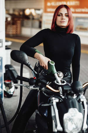 Positive girl sitting on her expensive urban bike. Custom sport motorcycle and its female owner. Vintage photo of refueling.の写真素材