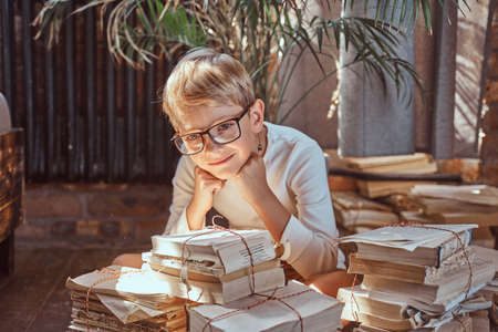Smart little boy poses sitting on floor near books looking at camera and smiling in relaxed living room.の写真素材
