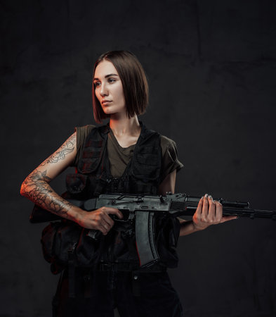 Holding assault rifle martial woman in black armour with short haircut poses in dark background.の写真素材