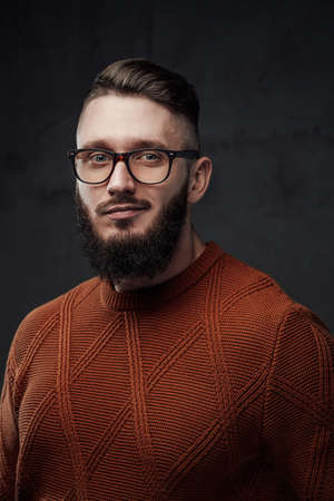 Portrait of a bearded and stylish guy with glasses he looks at camera smiling and posing in dark background.の写真素材