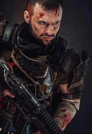 Holding custom shotgun apocalyptic bearded soldier in dark armour and with damaged head poses in dark background.の写真素材