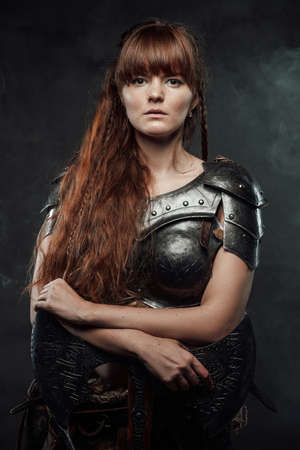 Barbaric beutiful woman from north armed with two handed axe and with brown hairs poses in dark foggy background.の写真素材