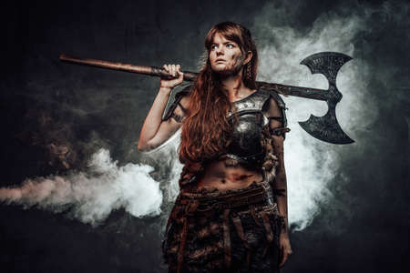 Portrait of woman viking wielding two handed axe and dressed in dark light armour in dark foggy...