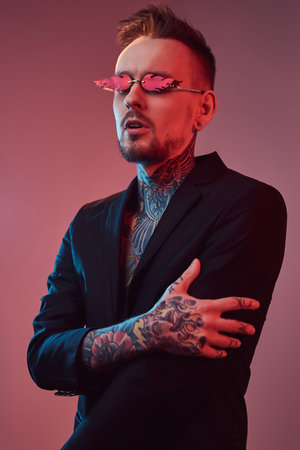 Portrait of a tattooed and fashionable hipster guy with stylish hairstyle in black suit weared with sunglasses poses in colourful background.の写真素材