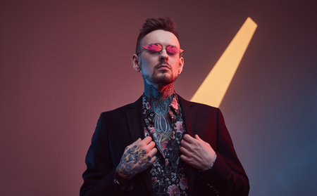 Weared with sunglasses stylish and tattooed businessperson with fashionable haircut and beard poses...